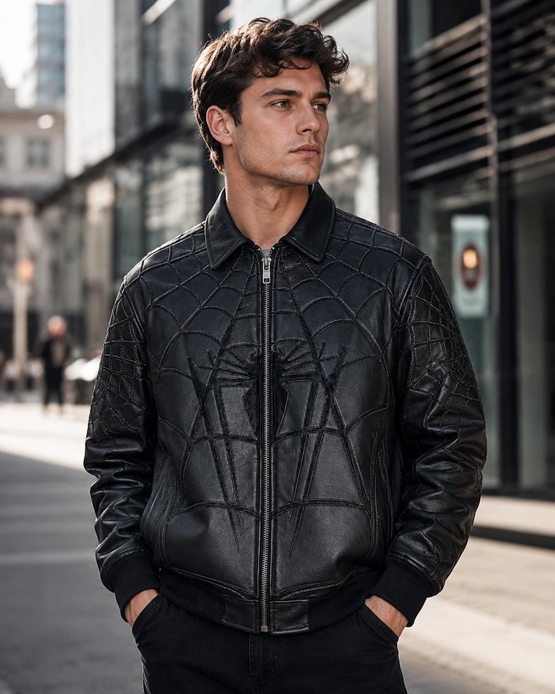 May include: A black leather bomber jacket featuring a prominent embossed spiderweb pattern across the front and sleeves, a classic collar, a full-length silver-toned metal zipper closure, and ribbed cuffs at the wrists and waist hem.
