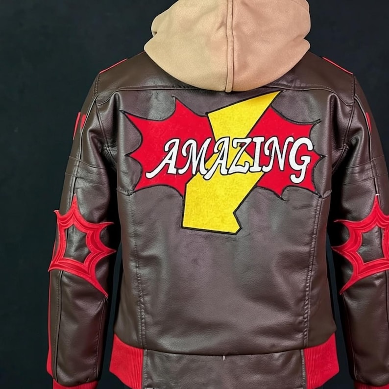 May include: A brown leather jacket with a tan hood, featuring a large red and yellow graphic on the back with the word AMAZING in white text. The sleeves have red star-shaped patches, and the jacket includes a red ribbed hem at the waist.