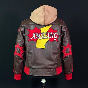 May include: A brown faux leather jacket with a tan hood, featuring a large red and yellow lightning bolt graphic on the back with the word AMAZING in white text. The jacket includes red ribbed cuffs and hem, with red star-shaped accents on sleeves.