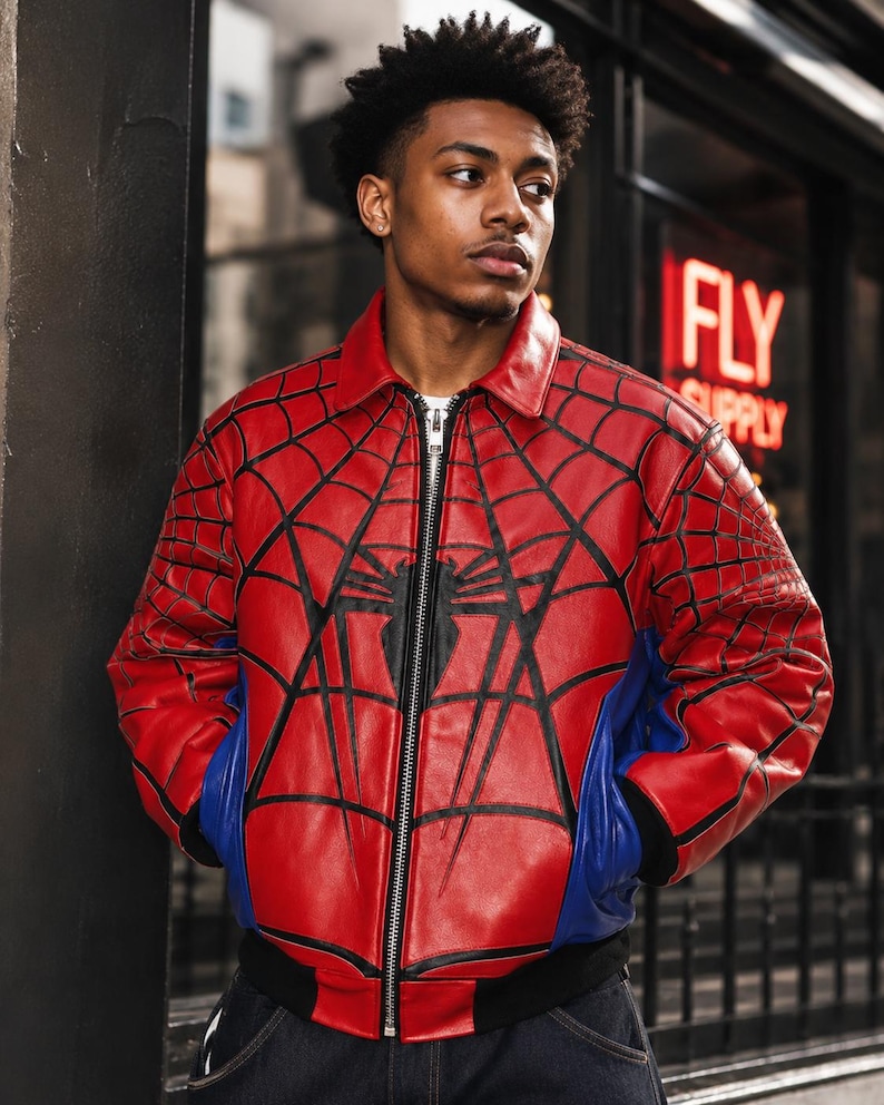 May include: A red and blue leather bomber jacket featuring a black spider web pattern across the chest and sleeves, a central black spider emblem, a silver front zipper, a classic collar, and black ribbed cuffs and hem at the waistline.