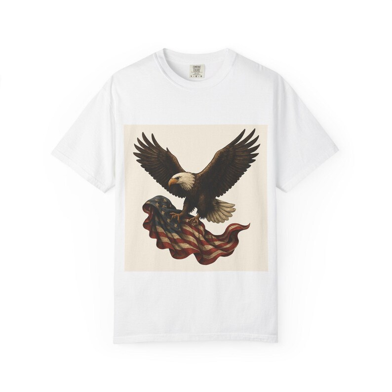 A white short-sleeved t-shirt with a graphic of a bald eagle with outstretched wings carrying a folded American flag in its talons.