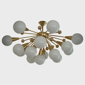May include: A mid-century modern Sputnik chandelier with a brass finish and multiple white globe lights. The fixture has a central hub with radiating arms, each holding a white globe.
