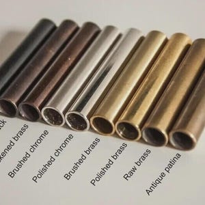 May include: A collection of cylindrical metal tubes in various finishes, including matte black, antique black, blackened brass, brushed chrome, polished chrome, brushed brass, polished brass, raw brass, and antique patina. Text labels identify each finish.
