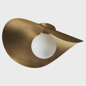May include: A brass-coloured, petal-shaped ceiling light fitting with a white, spherical light bulb in the centre. The fitting has a smooth, curved design and is mounted on a white background.