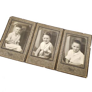 May include: A vintage photo album with three black and white photos of young boys. Each photo is framed with a brown border and has the text "Mocco Camera" printed on the bottom.