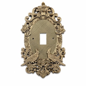 May include: An oval light switch plate with a metallic gold finish, featuring an ornate border of sculpted flowers and scrolling leaves. Two birds with crests are positioned at the bottom, facing each other. The center has a rectangular cutout.