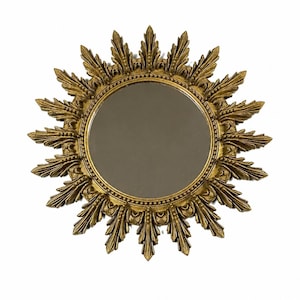 May include: A gold-colored sunburst mirror with a round, reflective center. The frame features ornate, leaf-like details radiating outwards. The mirror is designed to be mounted on a wall and adds a decorative touch to any room.