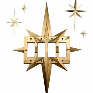 May include: A gold-coloured four-gang light switch wall plate featuring a starburst design with elongated points. The central rectangular plate is integrated into a large, multi-pointed star shape, accompanied by four smaller, separate star-shaped wall accents.