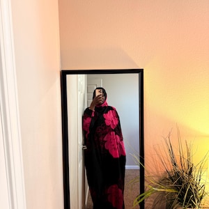 May include: A black robe with large pink floral patterns is reflected in a mirror. The robe appears to be made of a soft material and is worn by a person. The mirror has a black frame.