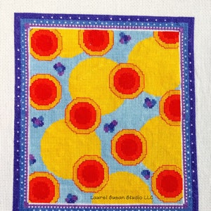 May include: A cross-stitch pattern with a blue background and yellow and red circles. The pattern is framed with a purple border with white dots. The text "Laurel Susan Studio LLC" is in the bottom right corner.