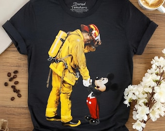 Könnte beinhalten: Ein schwarzes Kurzarm-T-Shirt mit einem Grafikdruck eines Feuerwehrmanns in gelber Schutzkleidung, der Händchen mit Mickey Mouse hält. Der Innenkragen enthält den Text Bored Teachers und eine Website-URL in weißem Druck.