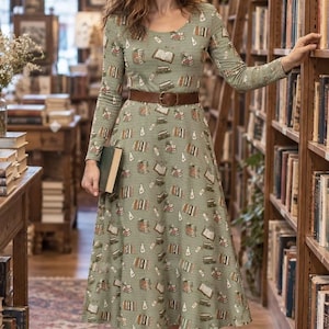 May include: A sage green long-sleeve midi dress featuring a repeating pattern of stacked books and reading glasses, cinched at the waist with a brown leather belt. The dress has a round neckline and a flared skirt that falls below the knees.