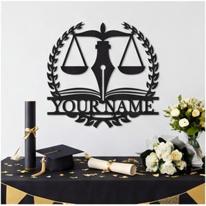 May include: A black wall-mounted sign featuring a central fountain pen nib, a pair of scales, and an open book, all enclosed within a circular laurel wreath. The text "YOUR NAME" is prominently displayed in a bold, sans-serif font across the center.