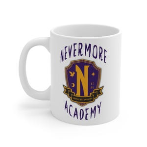 Può includere: Tazza in ceramica bianca con la scritta "NEVERMORE ACADEMY" in carattere gotico viola scuro. La tazza presenta uno stemma con una grande "N" dorata e la frase "UNITAS EST INVICTA" su uno stendardo.