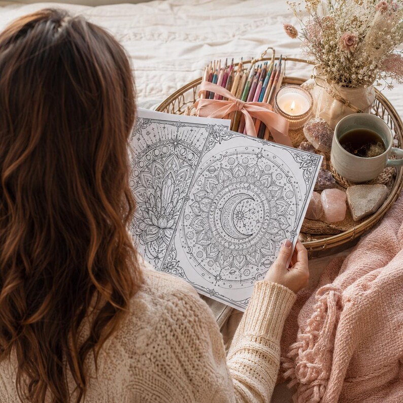 May include: Two white sheets of paper featuring intricate black line art illustrations of a crescent moon, stars, planets, and floral mandala patterns. The designs are detailed with geometric shapes and celestial motifs, presented as coloring pages.
