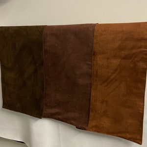 May include: A rectangular, multi-toned suede panel. The panel is divided into three vertical sections, each a different shade of brown, ranging from dark olive to a warm, reddish-brown. The suede has a soft, textured appearance.