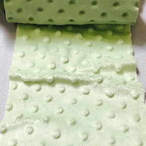 May include: A close-up of a light green fabric with a textured, dotted pattern. The fabric is soft and plush.