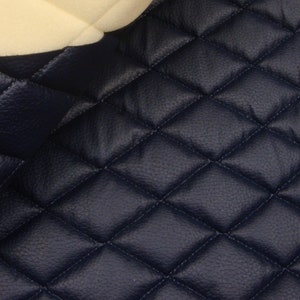 May include: Close-up of a dark blue quilted fabric with a diamond pattern. The fabric is soft and textured, and it has a subtle sheen.