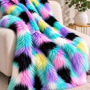 May include: A plush faux fur throw blanket featuring a vibrant, multi-colored pattern of long, shaggy fibers in shades of bright pink, electric blue, sunny yellow, deep purple, black, and white, arranged in a repeating, textured diagonal design.