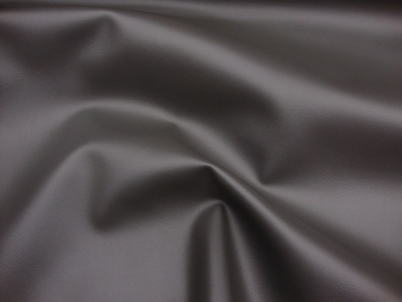 May include: A close-up of a smooth, dark grey fabric with a subtle texture. The fabric is draped and folded, creating soft curves and folds.