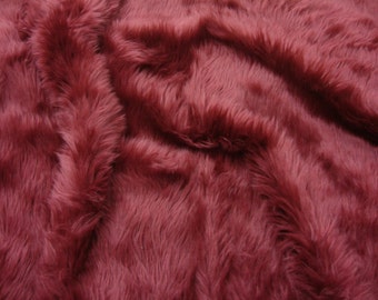 May include: Close-up of a soft, plush fabric in a deep burgundy color. The fabric has a long pile and a fuzzy texture.