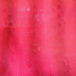 May include: A close-up of a bright pink fabric with a snakeskin pattern.