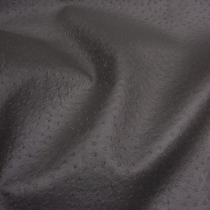 May include: Close-up of a dark gray textured fabric with a subtle pattern of small dots. The fabric has a soft, supple feel and a slightly pebbled surface.