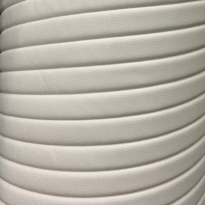 May include: Close-up of a white, textured, quilted fabric. The fabric has a subtle sheen and a slightly raised pattern.
