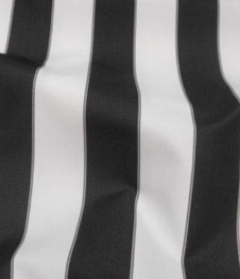 May include: Close-up of a fabric with vertical black and white stripes. The stripes are of varying widths, creating a bold, graphic pattern. The fabric appears to be smooth and possibly woven, with subtle variations in the light reflecting off the surface.