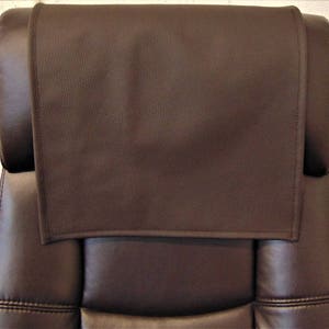 May include: A brown leather headrest for a chair. The headrest is rectangular and has a stitched edge.