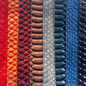 May include: A collection of leather samples in various colors and textures. The samples include white quilted leather, red, orange, and burgundy embossed leather, brown, silver, teal, blue, and black snake-skin patterned leather.