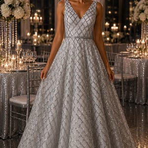 May include: A floor-length silver gown featuring a V-neckline and a sleeveless bodice. The dress is adorned with a repeating diamond-shaped grid pattern composed of shimmering silver sequins and beads, with a thin matching belt at the waist.