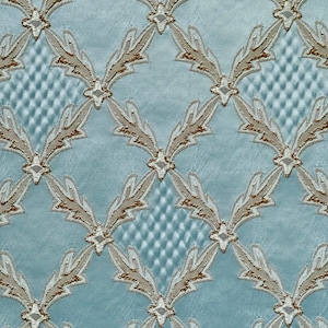 May include: A light blue fabric with a repeating pattern of gold and white stylized leaves. The leaves are arranged in a diamond shape and create a geometric design.