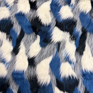 May include: Close-up of a faux fur fabric with a pattern of white, navy, and shades of blue. The fabric has a shaggy texture, with long, soft fibers. The design is abstract and resembles a camouflage pattern.