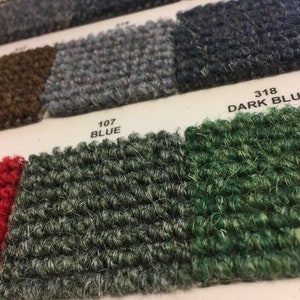 May include: Close-up of carpet samples in various colors, including dark blue, dark green, and light green. The samples are labeled with their corresponding numbers: 318 DARK BLU, 107 BLUE, 320 DARK GREEN, and LIGH.