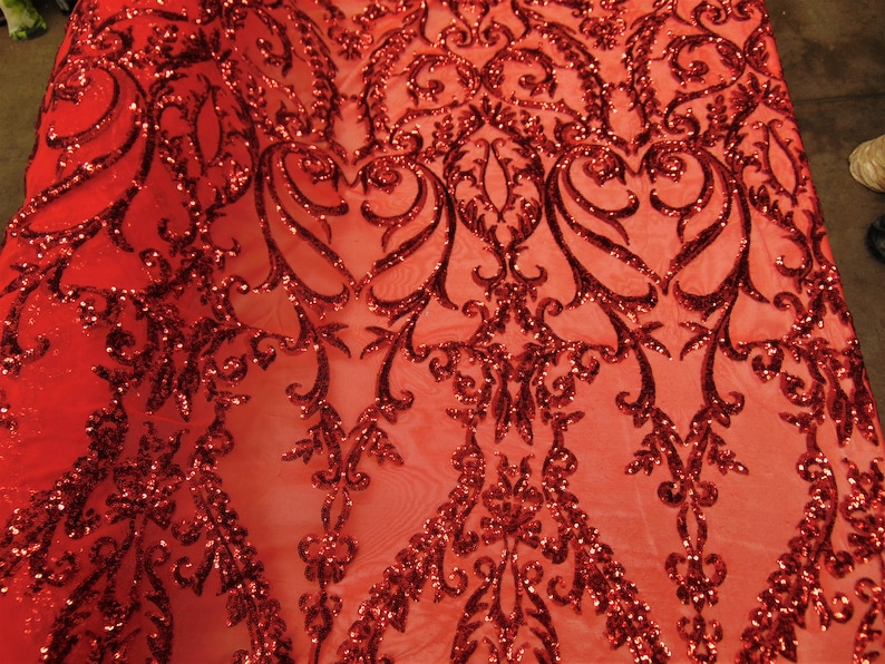 May include: Red sequin fabric with a damask pattern. The sequins are scattered throughout the fabric, creating a sparkly effect.