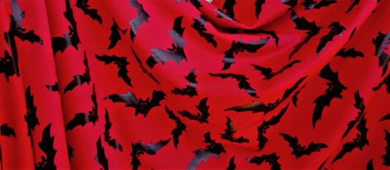 以下が含まれることがあります： 赤い生地に黒いコウモリの模様がプリントされています。コウモリは生地にランダムに散らばっています。