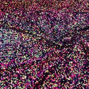 May include: A close-up of a fabric with iridescent sequins in shades of pink, purple, and gold. The sequins are densely packed together, creating a shimmering effect.