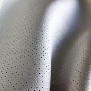 K&ouml;nnte beinhalten: Ein wei&szlig;es Material mit einem gleichm&auml;&szlig;igen Muster aus kleinen, regelm&auml;&szlig;ig angeordneten kreisf&ouml;rmigen Perforationen. Die Oberfl&auml;che weist eine feine, subtile Textur auf und ist in weichen Kurven drapiert, die Tiefe und Licht betonen.