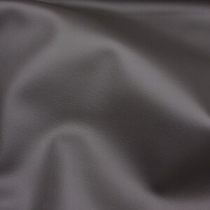 May include: A close-up of a smooth, grey fabric with a subtle texture. The fabric is draped and folded, creating soft curves and folds.
