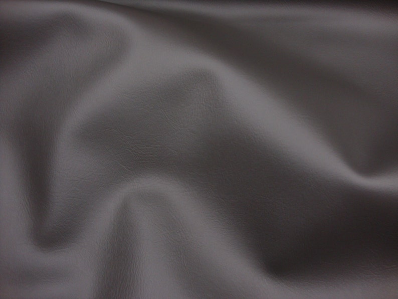 May include: A close-up of a smooth, grey fabric with a subtle texture. The fabric is draped and folded, creating soft curves and folds.