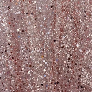 May include: A close-up of a fabric with a delicate, sheer texture. The fabric is covered in small, iridescent sequins that shimmer in the light. The sequins are arranged in a random pattern, creating a sparkling and glamorous effect.