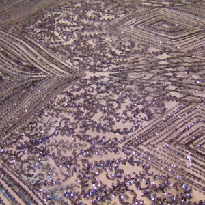 May include: Purple and silver sequined fabric with a geometric pattern. The fabric has a delicate, sheer texture and is perfect for adding a touch of sparkle to any project.