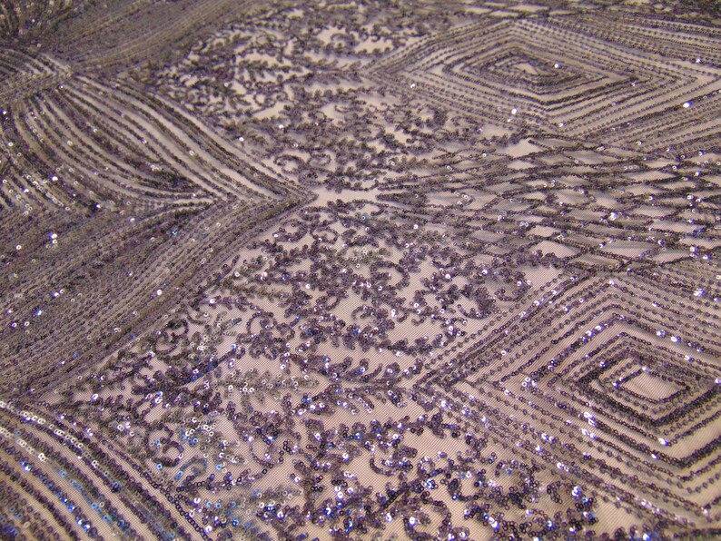May include: Purple and silver sequined fabric with a geometric pattern. The fabric has a delicate, sheer texture and is perfect for adding a touch of sparkle to any project.