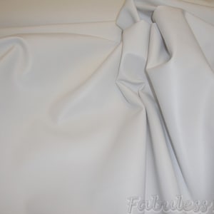 May include: White faux leather fabric. The fabric is smooth and has a slight sheen. It is perfect for upholstery, crafts, and other projects.