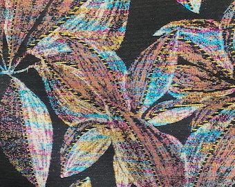 May include: Close-up of a black fabric with a metallic floral pattern in shades of gold, blue, and pink. The fabric has a textured, woven look.