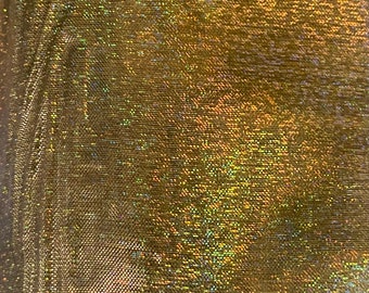 Könnte beinhalten: Nahaufnahme eines schimmernden, goldenen Stoffes mit einem strukturierten, gewebten Muster. Das Material hat einen glitzernden, irisierenden Effekt, der das Licht mit einem Farbspektrum reflektiert. Der Stoff scheint leicht und möglicherweise für Kleidung oder Dekorationszwecke verwendet zu werden.