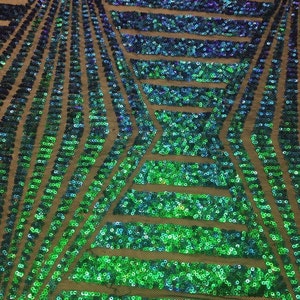 May include: Close-up of a fabric with a geometric pattern of sequins. The sequins transition from green to blue and purple, creating a shimmering effect. The fabric is likely used for apparel or decorative purposes.