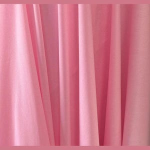 May include: A close-up of a pink fabric with vertical folds. The fabric has a soft, matte appearance and a consistent color throughout. The folds create shadows and highlights, adding depth to the image. The overall effect is smooth and elegant.