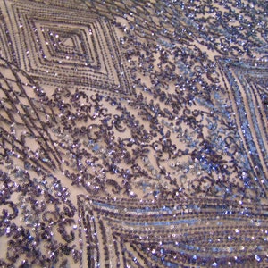 May include: A close-up of a fabric with a geometric pattern of sequins in shades of blue and purple. The sequins are arranged in a diamond pattern, creating a shimmering effect.